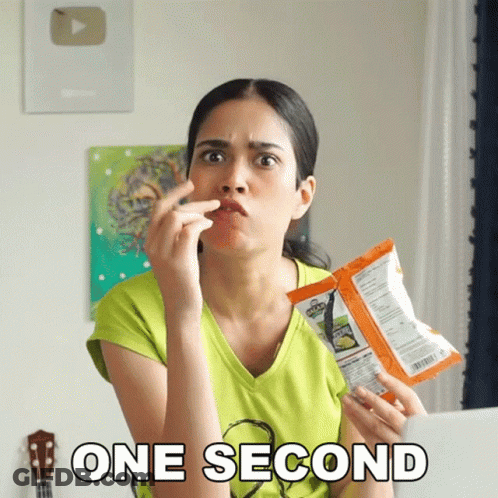 A Woman Is Holding A Bag Of Chips And The Words One Second Are Above Her GIF