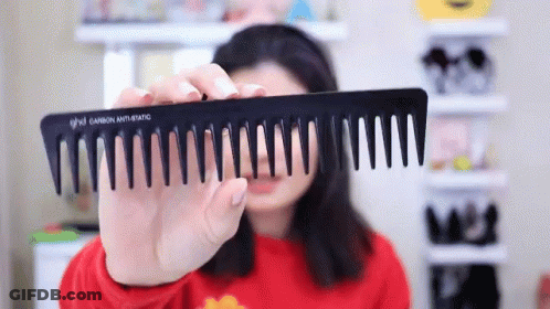 A Woman Is Holding A Black Comb That Says Ghd GIF