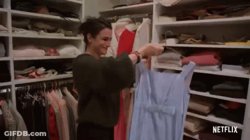 A Woman Is Holding A Blue Dress In A Closet Filled With Clothes . GIF