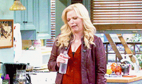 A Woman Is Holding A Bottle Of Water In Her Hand In A Kitchen GIF