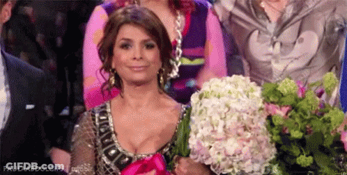 A Woman Is Holding A Bouquet Of Flowers In Her Hands While Sitting In A Crowd . GIF