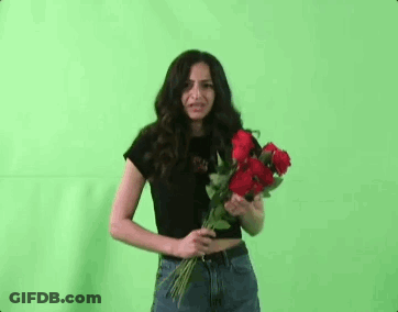 A Woman Is Holding A Bouquet Of Red Roses In Front Of Her Face Against A Green Screen . GIF