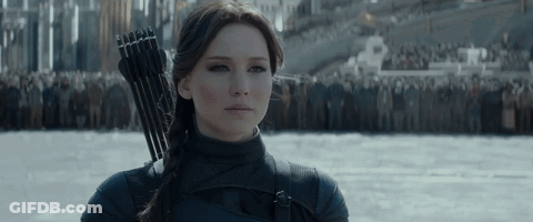 A Woman Is Holding A Bow And Arrow In Front Of A Crowd Of People GIF