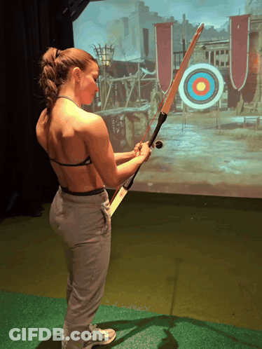 A Woman Is Holding A Bow And Arrow In Front Of A Screen That Says Uo On It GIF