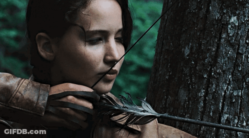 A Woman Is Holding A Bow And Arrow With A Feather In Her Mouth GIF
