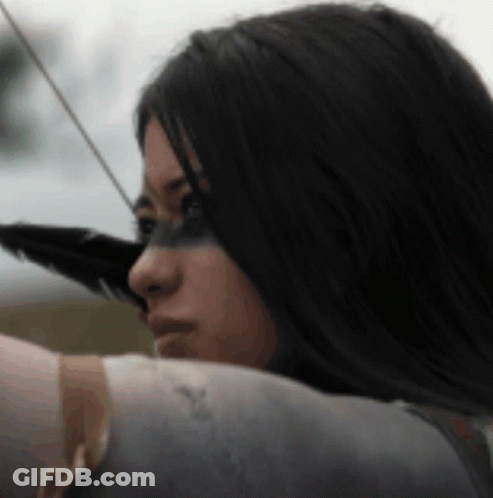 A Woman Is Holding A Bow And Arrow With A Feather On Her Face . GIF