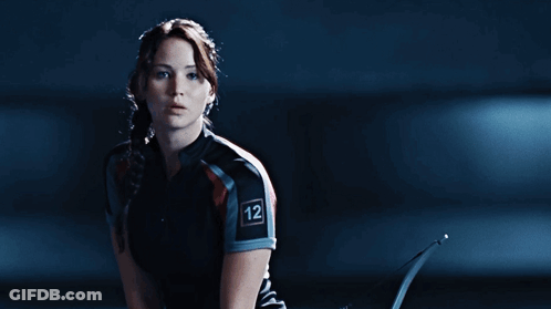 A Woman Is Holding A Bow And Arrow With The Word Hunger Games On Her Shirt GIF