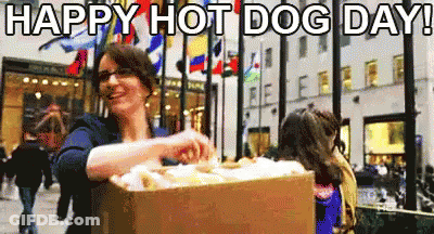 A Woman Is Holding A Box Of Hot Dogs In Front Of A Crowd Of People . GIF
