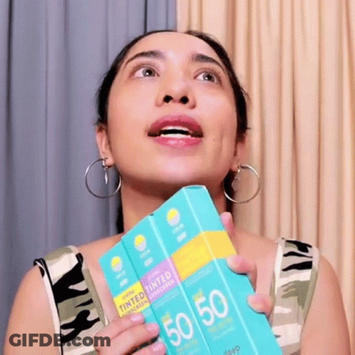 A Woman Is Holding A Box Of Tinted Sunscreen In Her Hand . GIF
