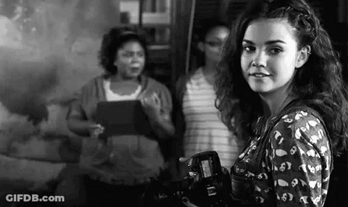 A Woman Is Holding A Camera In Front Of A Group Of Women . GIF