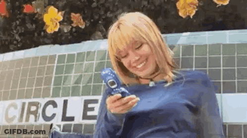 A Woman Is Holding A Cell Phone In Front Of A Building . GIF