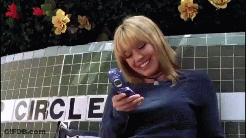 A Woman Is Holding A Cell Phone In Front Of A Circle Sign GIF
