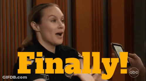 A Woman Is Holding A Cell Phone In Front Of A Sign That Says Finally On It GIF