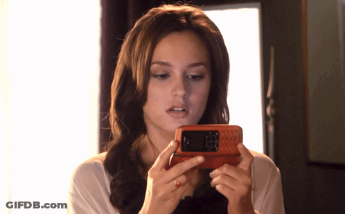 A Woman Is Holding A Cell Phone In Her Hands And Looking At The Screen GIF