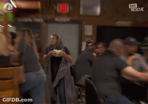 A Woman Is Holding A Drink In Front Of A Bar Rescue Sign GIF