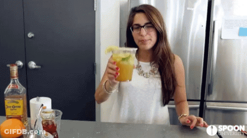 A Woman Is Holding A Drink In Front Of A Spoon University Sign GIF