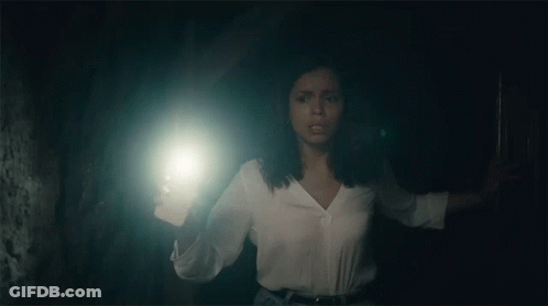 A Woman Is Holding A Flashlight In Her Hand In A Dark Room . GIF