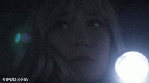 A Woman Is Holding A Flashlight In The Dark And Looking Up . GIF
