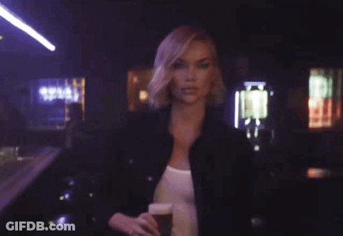 A Woman Is Holding A Glass Of Beer With The Words Hold My Beer Behind Her GIF