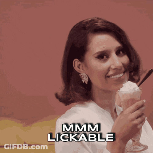 A Woman Is Holding A Glass Of Milkshake With Whipped Cream And The Words Mmmm Lickable Below Her GIF