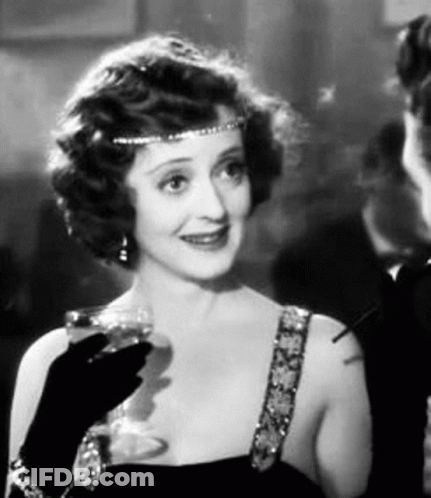 A Woman Is Holding A Glass Of Wine And Smoking A Cigarette . GIF