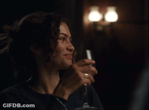 A Woman Is Holding A Glass Of Wine In A Dark Room GIF