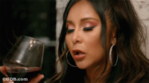 A Woman Is Holding A Glass Of Wine In Her Hand . GIF