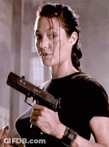 A Woman Is Holding A Gun In Her Hand And Looking At The Camera . GIF