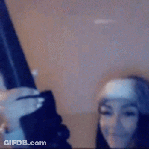 A Woman Is Holding A Gun In Her Hand And Smiling . GIF