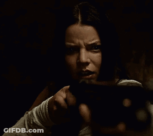 A Woman Is Holding A Gun In Her Hand In A Dark Room And Pointing At The Camera . GIF