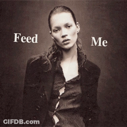 A Woman Is Holding A Hamburger And French Fries With The Words Feed Me Behind Her GIF