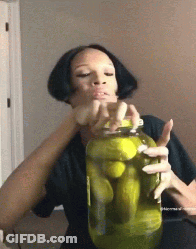 A Woman Is Holding A Jar Of Pickles In Her Hands . GIF