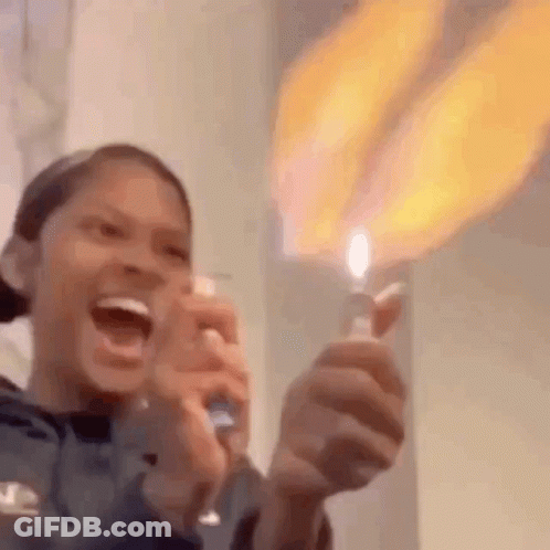 A Woman Is Holding A Lighter With A Flame Coming Out Of It And Laughing . GIF