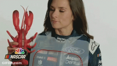 A Woman Is Holding A Lobster In Front Of A Nascar Sign GIF