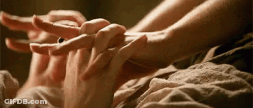 A Woman Is Holding A Man 'S Hand While Laying On A Bed . GIF