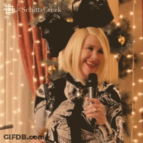 A Woman Is Holding A Microphone And Smiling In Front Of A Christmas Tree .. GIF