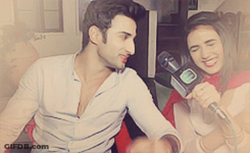 A Woman Is Holding A Microphone And Smiling While A Man Looks On GIF