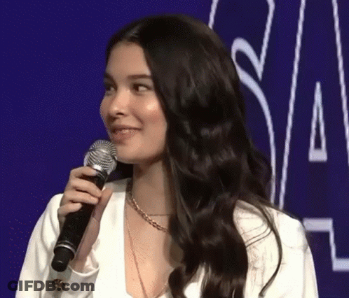 A Woman Is Holding A Microphone And Smiling While Standing In Front Of A Purple Background . GIF