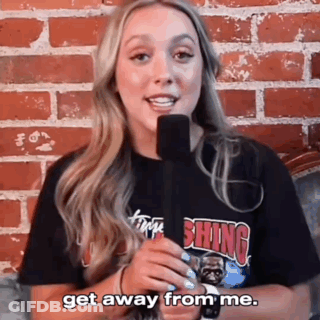 A Woman Is Holding A Microphone In Front Of A Brick Wall And Saying Get Away From Me . GIF