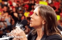 A Woman Is Holding A Microphone In Front Of A Crowd And Talking Into It . GIF