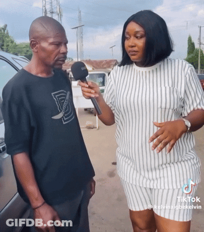 A Woman Is Holding A Microphone While Talking To A Man With A Black Shirt That Says D On It GIF