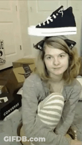 A Woman Is Holding A Pair Of Black Converse Shoes On Her Head . GIF