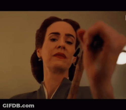 A Woman Is Holding A Pair Of Scissors And Looking At The Camera . GIF