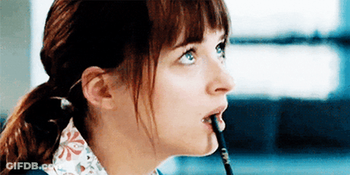 A Woman Is Holding A Pencil In Her Mouth . GIF