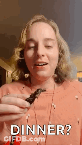 A Woman Is Holding A Piece Of Food In Her Hand And Saying `` Dinner ? '' . GIF