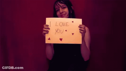 A Woman Is Holding A Piece Of Paper That Says I Love You GIF