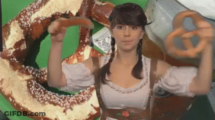 A Woman Is Holding A Pretzel In Front Of A Large Pretzel On A Green Screen . GIF