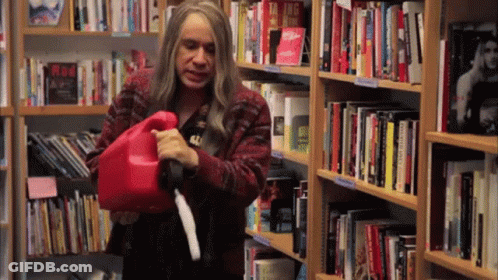 A Woman Is Holding A Red Gas Can In Front Of A Bookshelf With A Book Titled Taking Risks On It GIF