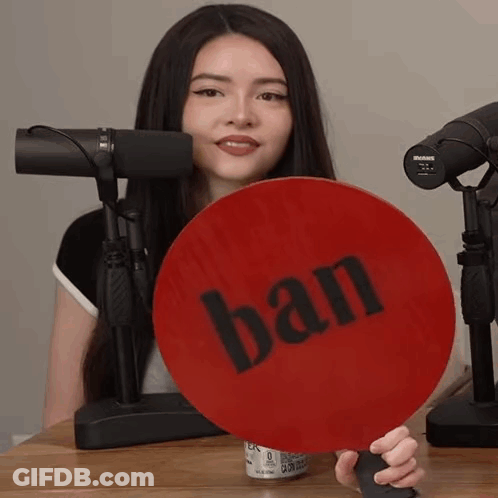 A Woman Is Holding A Sign That Says Ban In Front Of A Microphone GIF