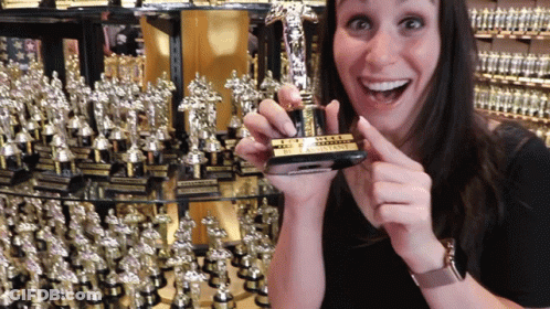 A Woman Is Holding A Small Trophy That Says " The Assistant " GIF